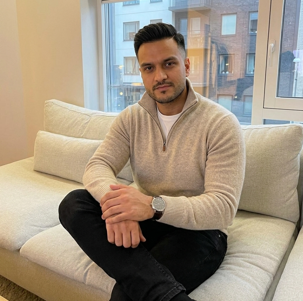 Ray Voice — Press Photo 2 — Ray Voice sitting indoors, wearing an oatmeal sweater and black jeans with an A. Lange & Söhne watch.